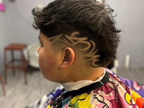 Perfil lateral de persona con cabello oscuro corto y diseño de degradado intrincado en los costados, usando camisa colorida