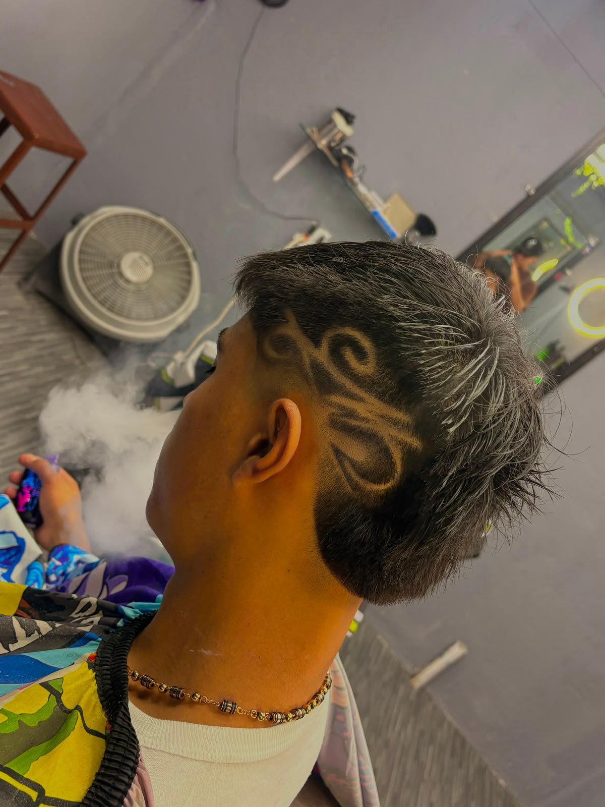 Persona con diseño de tatuaje tribal decorativo en la parte posterior de la cabeza y cuello, usando collar de cadena con cuentas