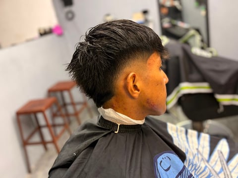 Perfil lateral de una persona con corte de cabello corto oscuro degradado en una barbería